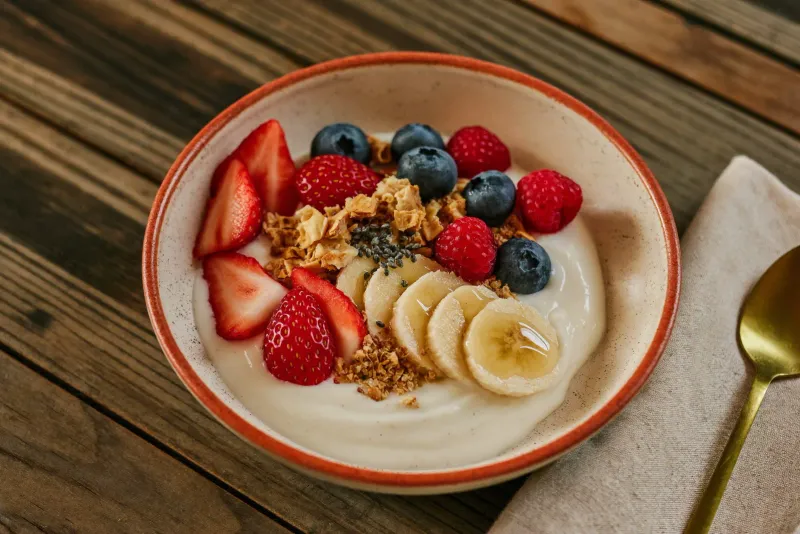 Bowl de iogurte natural coberto com frutas vermelhas, banana e granola dourada